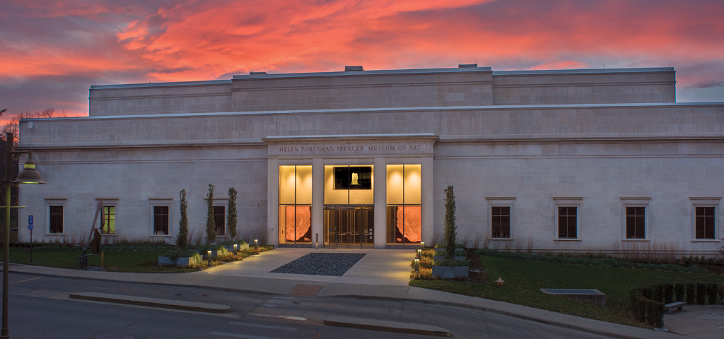 Image of the front of the Spencer Museum of Art taken at sunset so the background is filled with pink, red, orange, and deep violet hues.